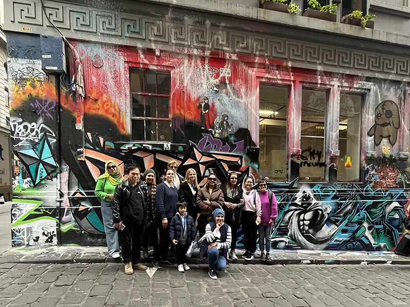 A group of Prace students stand in front of graffiti on the walls of a building in Hosier Lane.