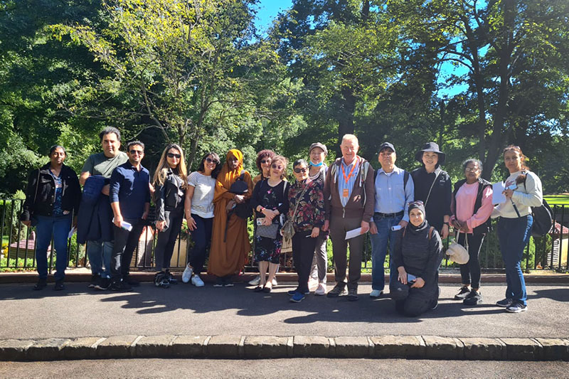 A group of EAL students and their teachers standing together on a path with Fitzroy Gardens behind them